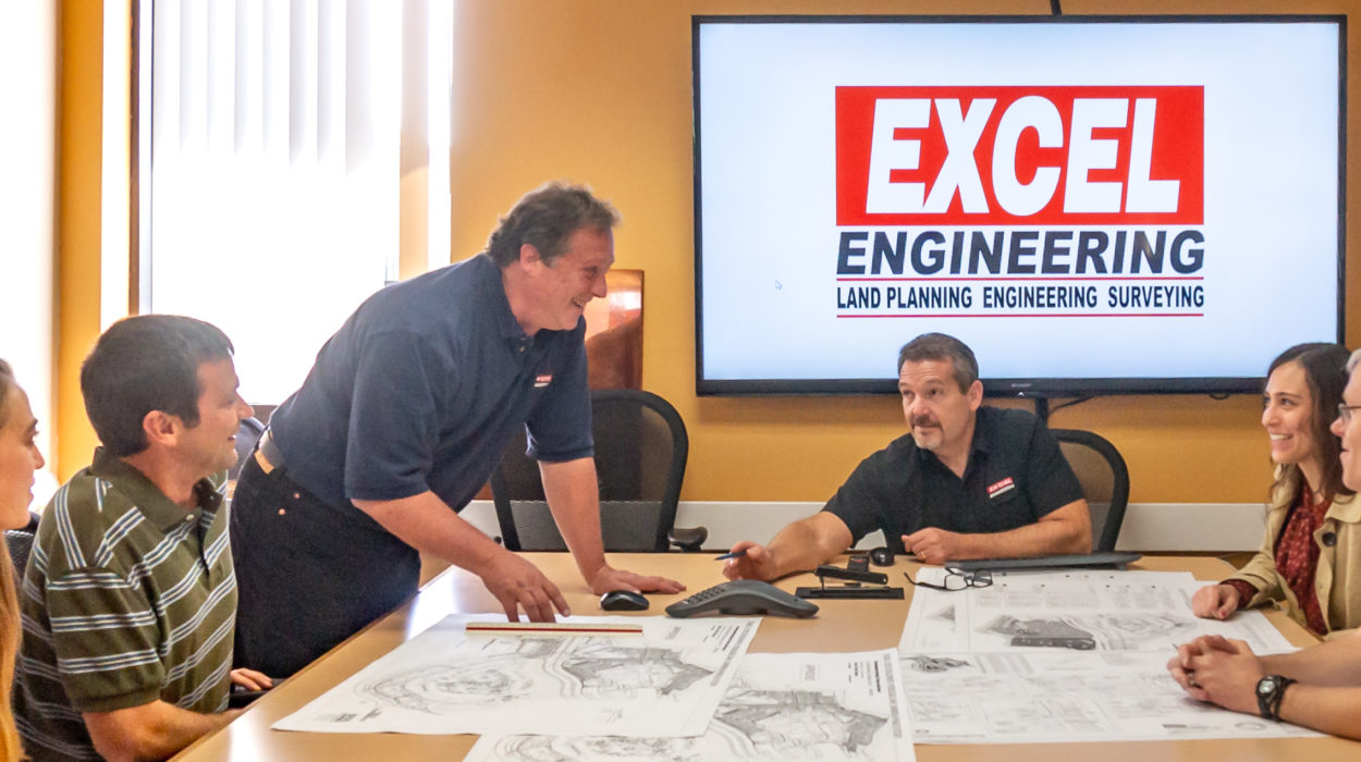 Photo of the Excel Engineering team meeting at a conference table planning out a design while smiling at each other.